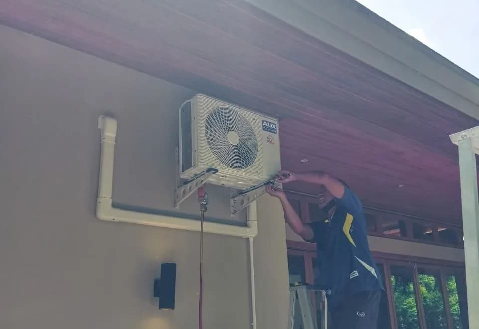 Technician mounting an outdoor air conditioning unit on a Phuket villa