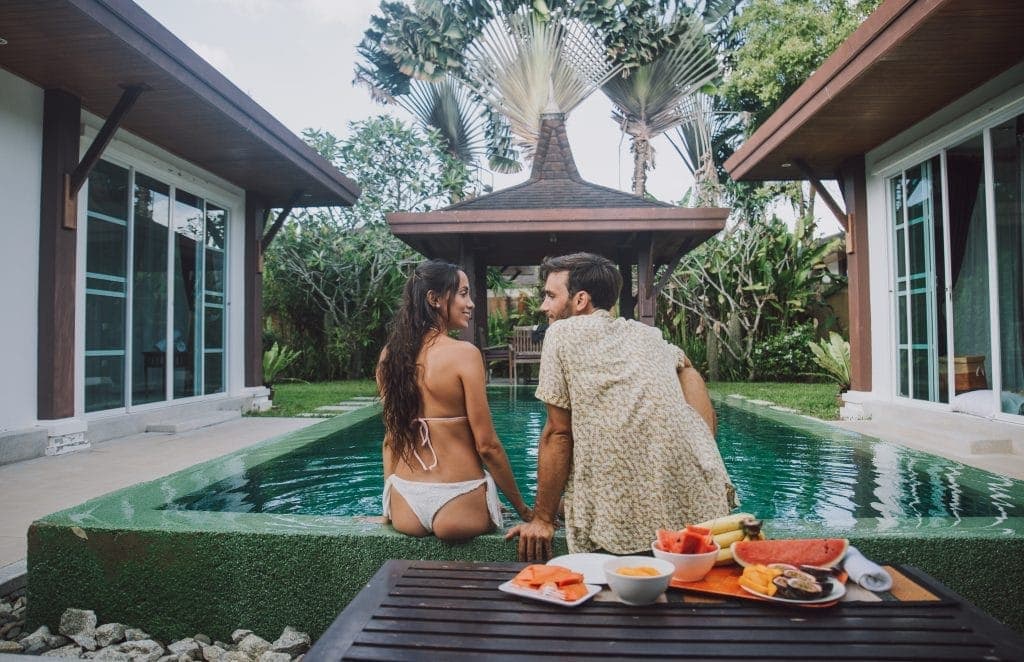 Un couple se détendant au bord d'une piscine privée dans un cadre de villa tropicale, avec des fruits frais sur une table à proximité