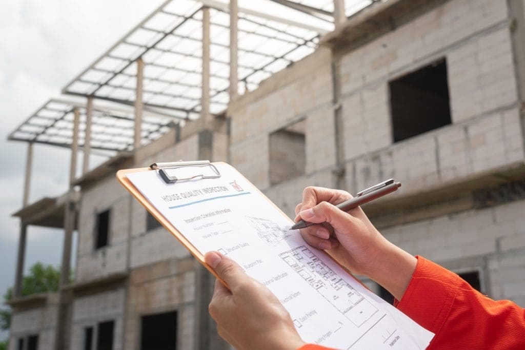 Chantier de construction avec un ingénieur ou un inspecteur prenant des notes sur un formulaire d'inspection de la qualité d'une maison
