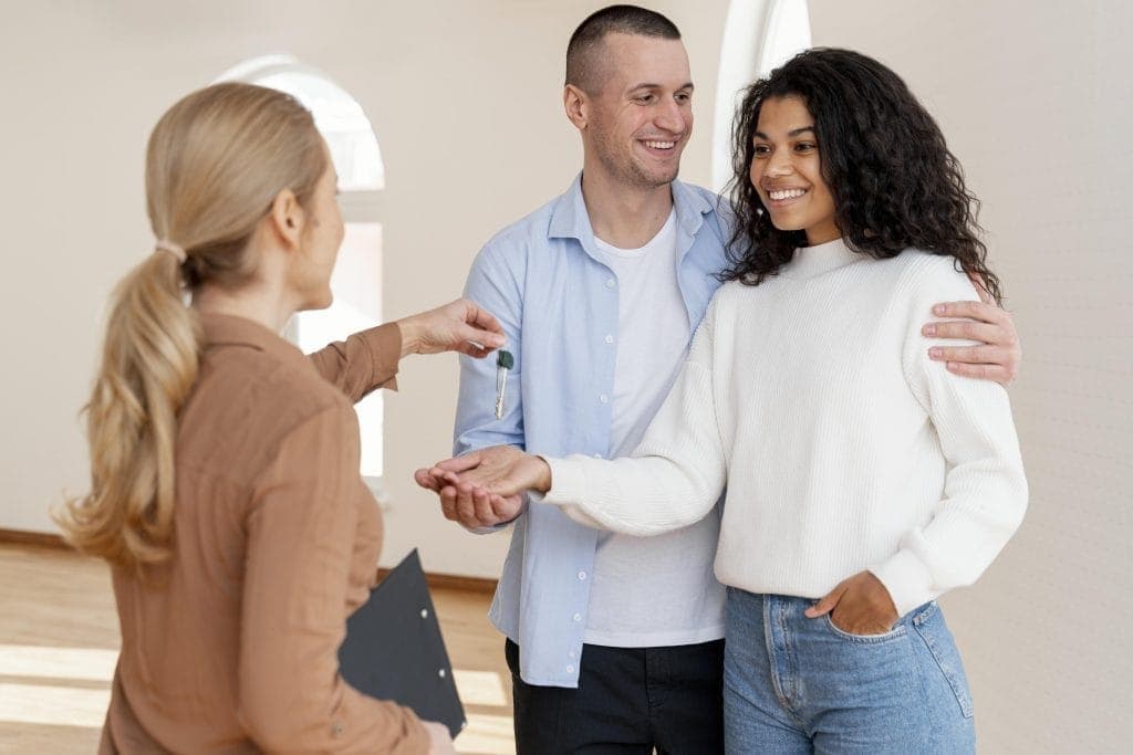 Happy couple receiving house keys from a property manager in a bright, empty room in order to use the service and management for the property